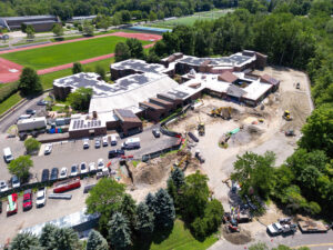 default - Waveny Aerial view of a construction site next to a school or campus building, with heavy equipment, dug earth, and a parking lot in the foreground.