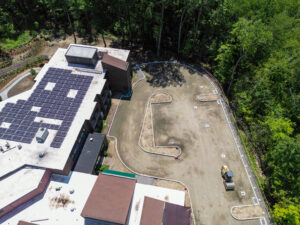 default - Waveny Aerial view of a building roof covered with solar panels, next to a curved concrete driveway and dense green trees nearby.