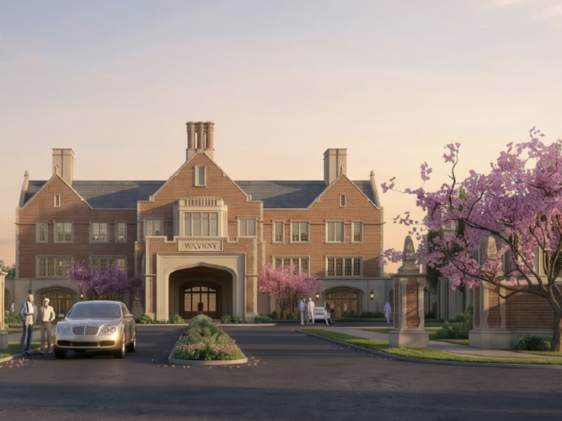 Brick mansion with arched entrance, flanked by pink blossoming trees and a car in the driveway.